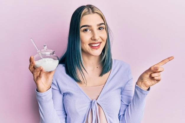 Smiling woman with blue hair holding a jar of sugar and pointing to the side