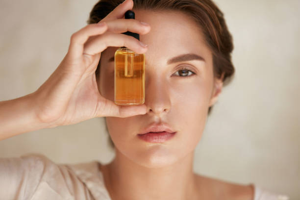 Portrait of a young woman holding a small amber glass bottle in front of her eye