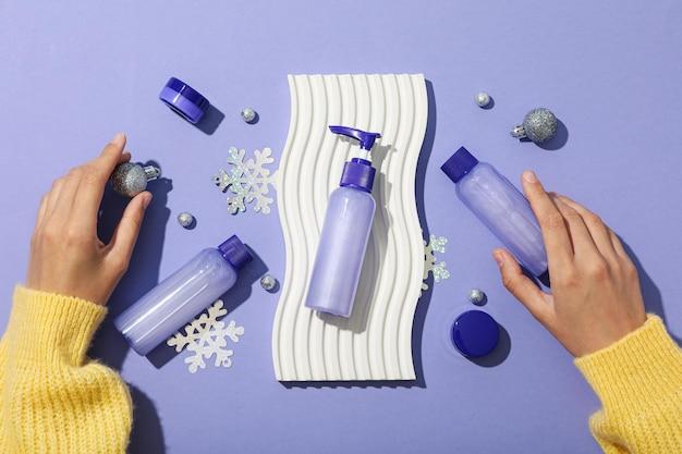 Hands arranging skincare products with snowflakes on a purple background