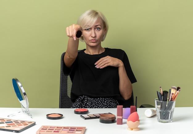 Woman doing makeup tutorial with various cosmetics on table