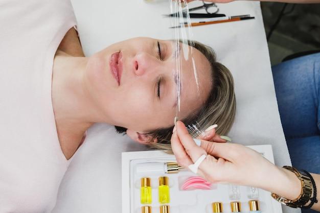 A woman receiving facial acupuncture treatment, with several needles on her face, lying down while a practitioner applies the treatment.