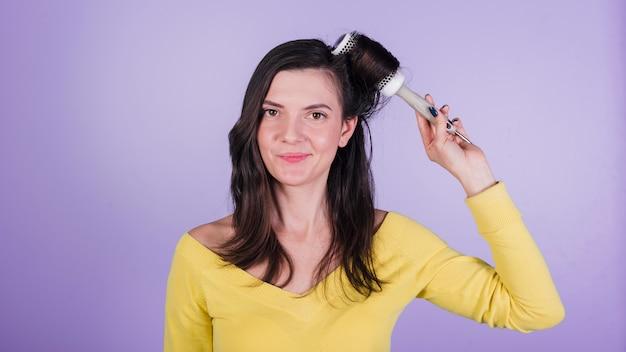 Woman styling her hair with round brush on purple background