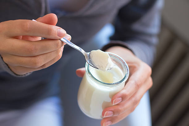 Person eating yogurt from a small glass jar with a spoon