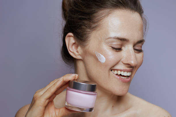 Happy woman applying moisturizing cream on her face